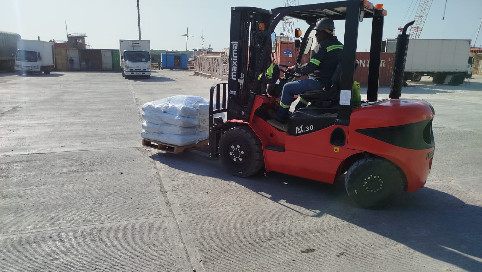 Un operario maneja una montacarga roja transportando un pallet con sacos blancos.