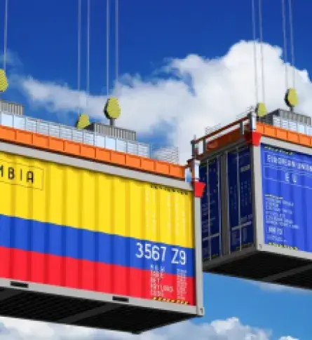 Contenedores de carga en el aire, uno con los colores de la bandera de Colombia, simbolizando comercio internacional.