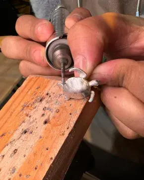 Las manos de un orfebre colombiano esculpen una pieza de arte con forma de tortuga.