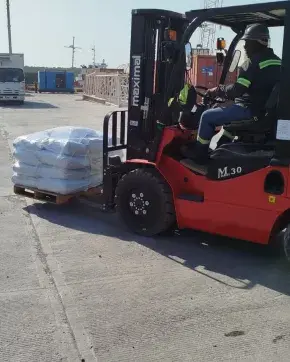 Un operario maneja una montacarga roja transportando un pallet con sacos blancos.