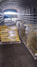Bultos de cemento conductivo empacados en bolsas amarillas, organizados sobre estibas y envueltos en plástico, dentro de un camión tipo furgón.
