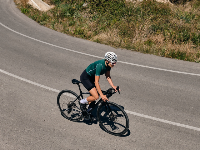 Colombian cyclist wearing women's sportswear, road cycling helmets, cycling gloves and cycling jacket on a mountain road near to a Colombian town.