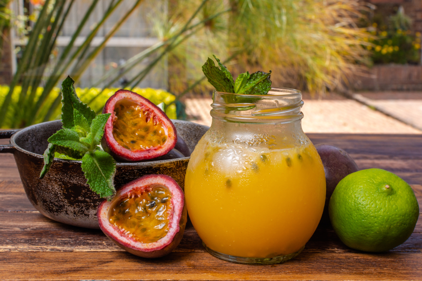 jugo de gulupa junto a frutos de gulupa sobre una mesa durante un día de sol.